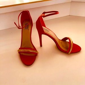 Orange/red high heeled sandal with a gold embellished toe strap. 3.5” heels